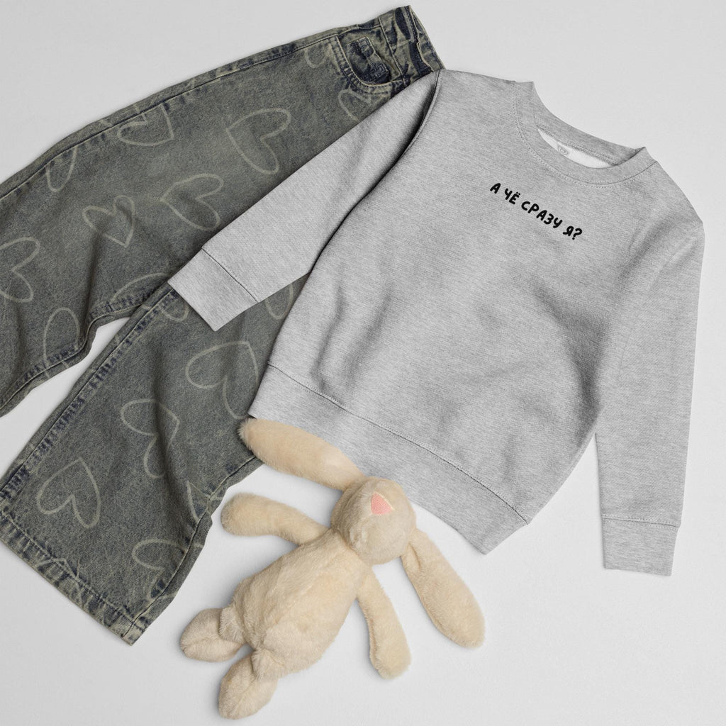 May include: A light gray long-sleeve sweatshirt with the black text "А ЧЁ СРАЗУ Я?" printed on the chest, paired with dark gray denim jeans featuring a white heart pattern and a small, light beige plush rabbit toy with long ears.